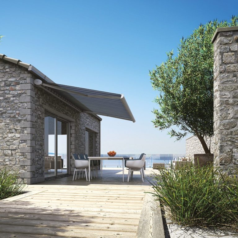 kadeco.de zu sehen ist eine Terrasse an einem Natursteinhaus und einer ausgefahrenen Markise von dem Hersteller Kadeco